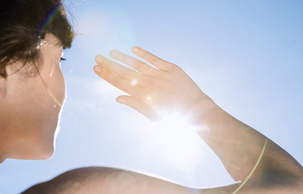 Una mujer se protege los ojos del sol con la mano derecha.