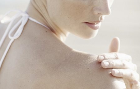 Mujer aplicándose crema en el hombro derecho.